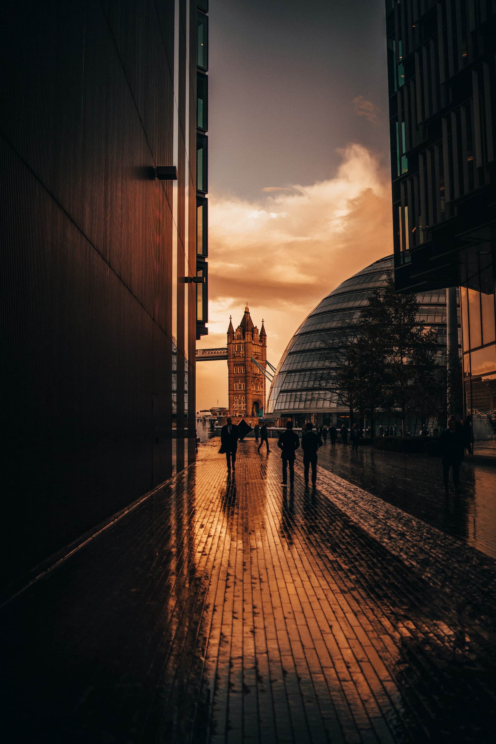 People walking a London street at golden hour beneath the city skyline and a glowing dusk sky