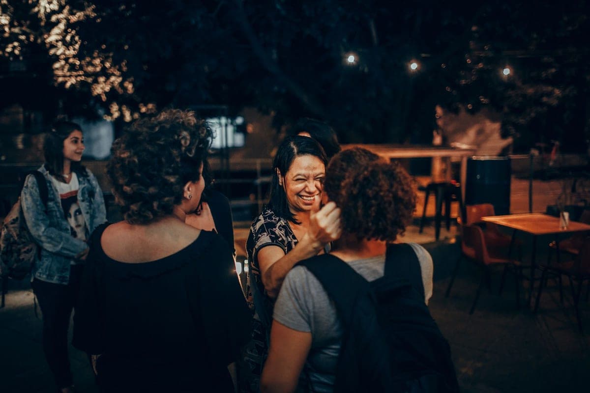 Friends laughing together over drinks at an outdoor cafe in the evening, warm string lights glowing behind them