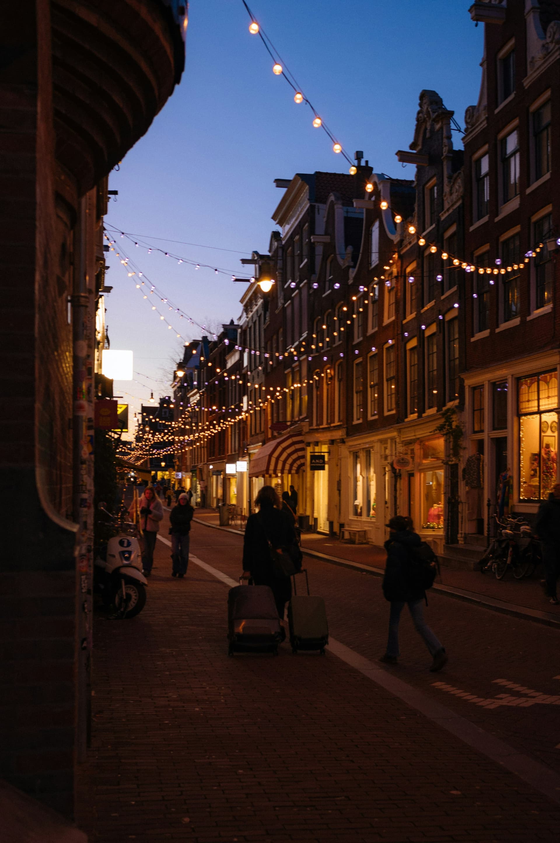 People strolling a London street strung with warm festoon lights on a calm evening