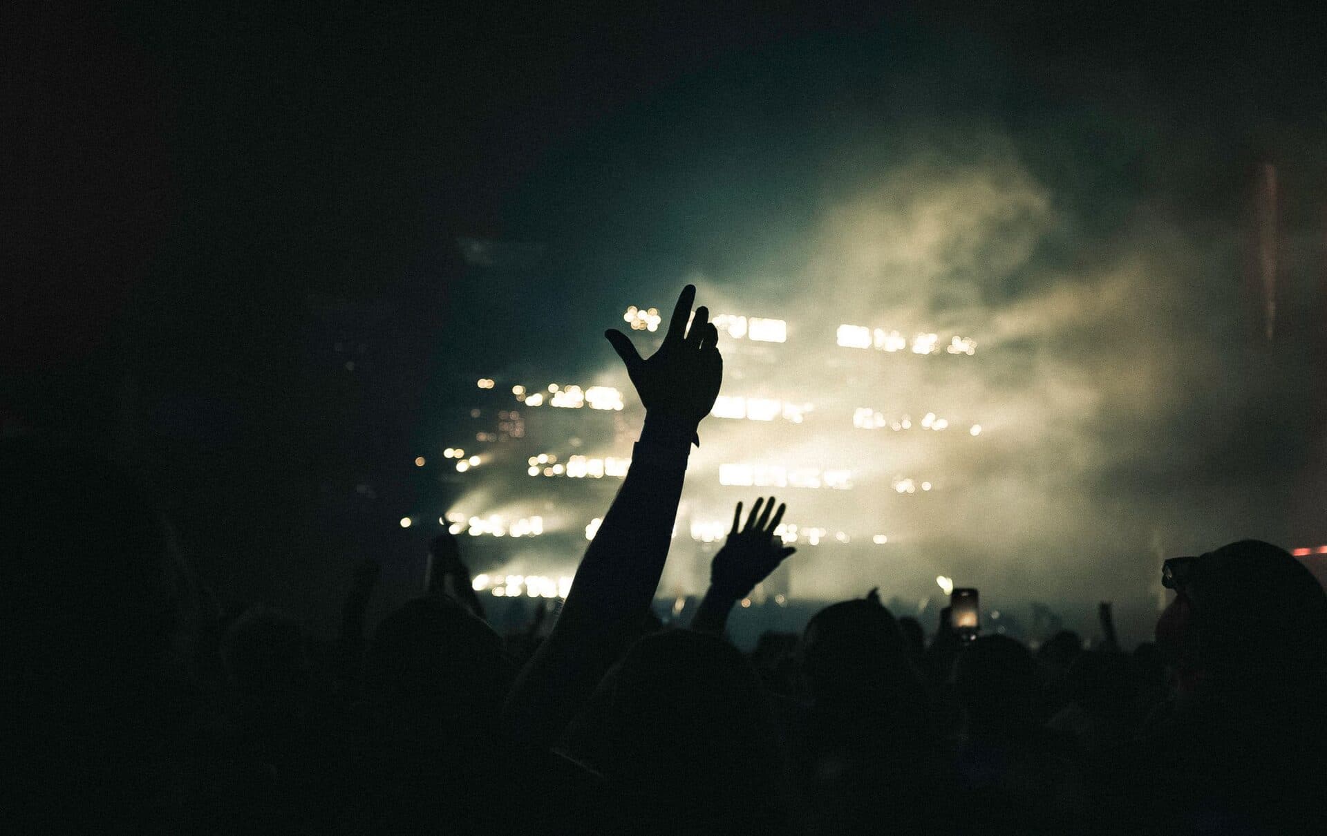 A buzzing crowd in silhouette with hands raised against a haze of warm stage light and drifting smoke at a London night out