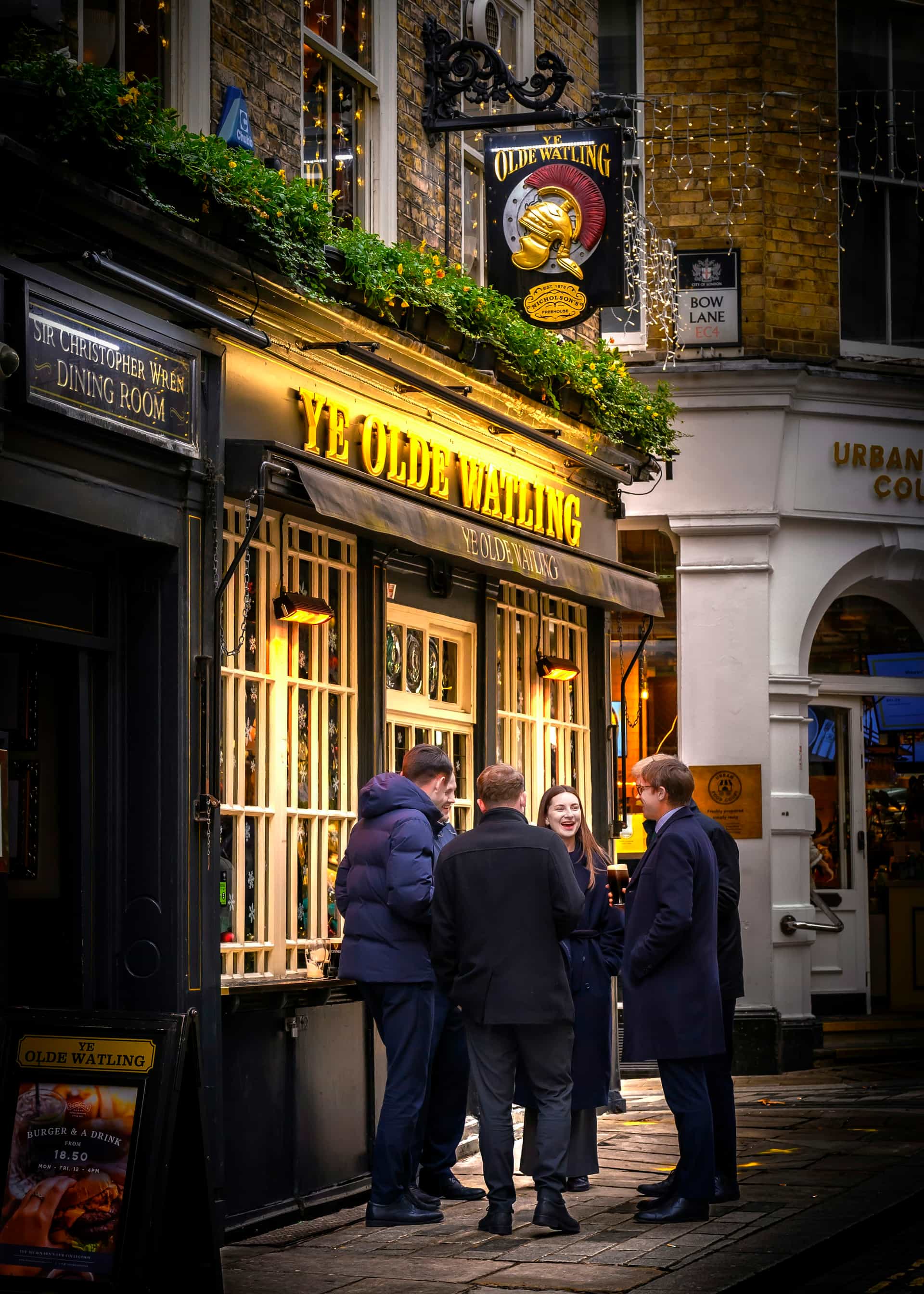 Friends gathered outside Ye Olde Watling, a characterful City of London pub glowing on an evening street
