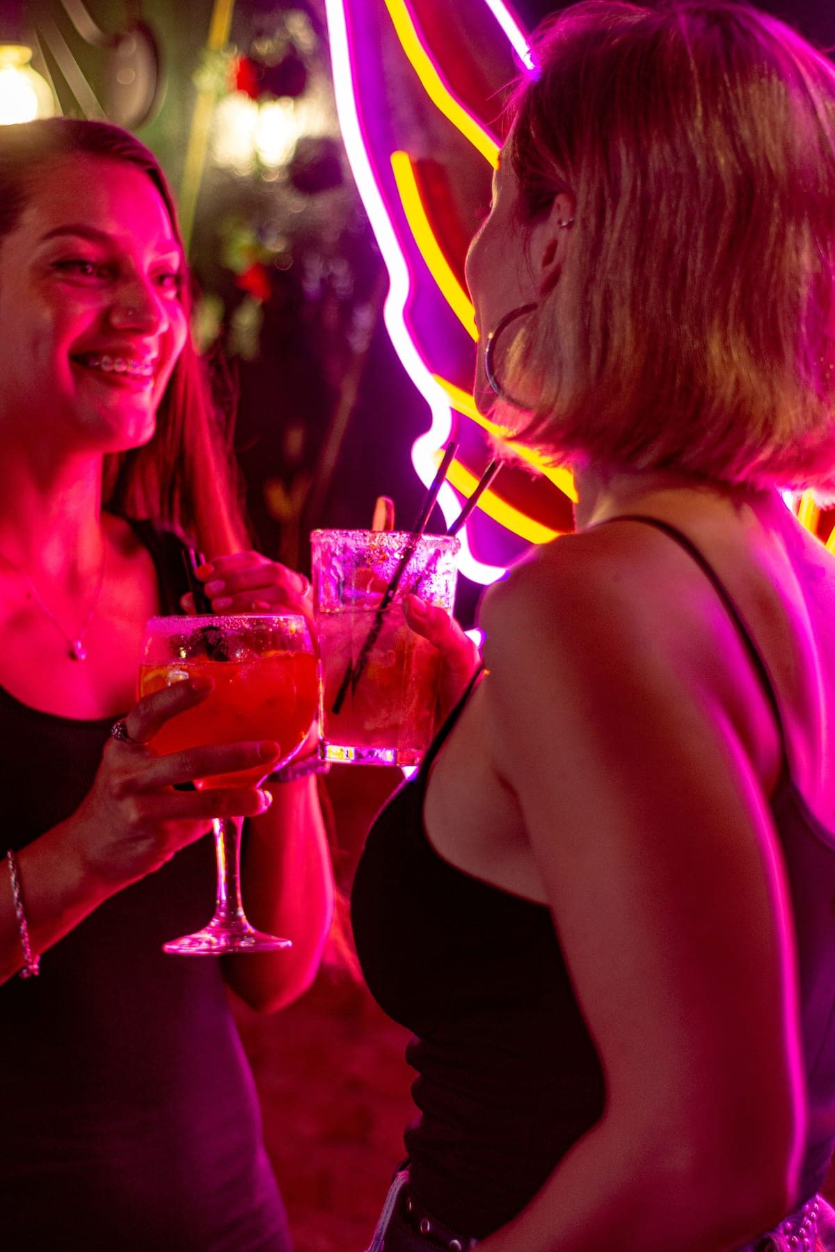 Two friends laughing together over cocktails under warm neon light on a night out