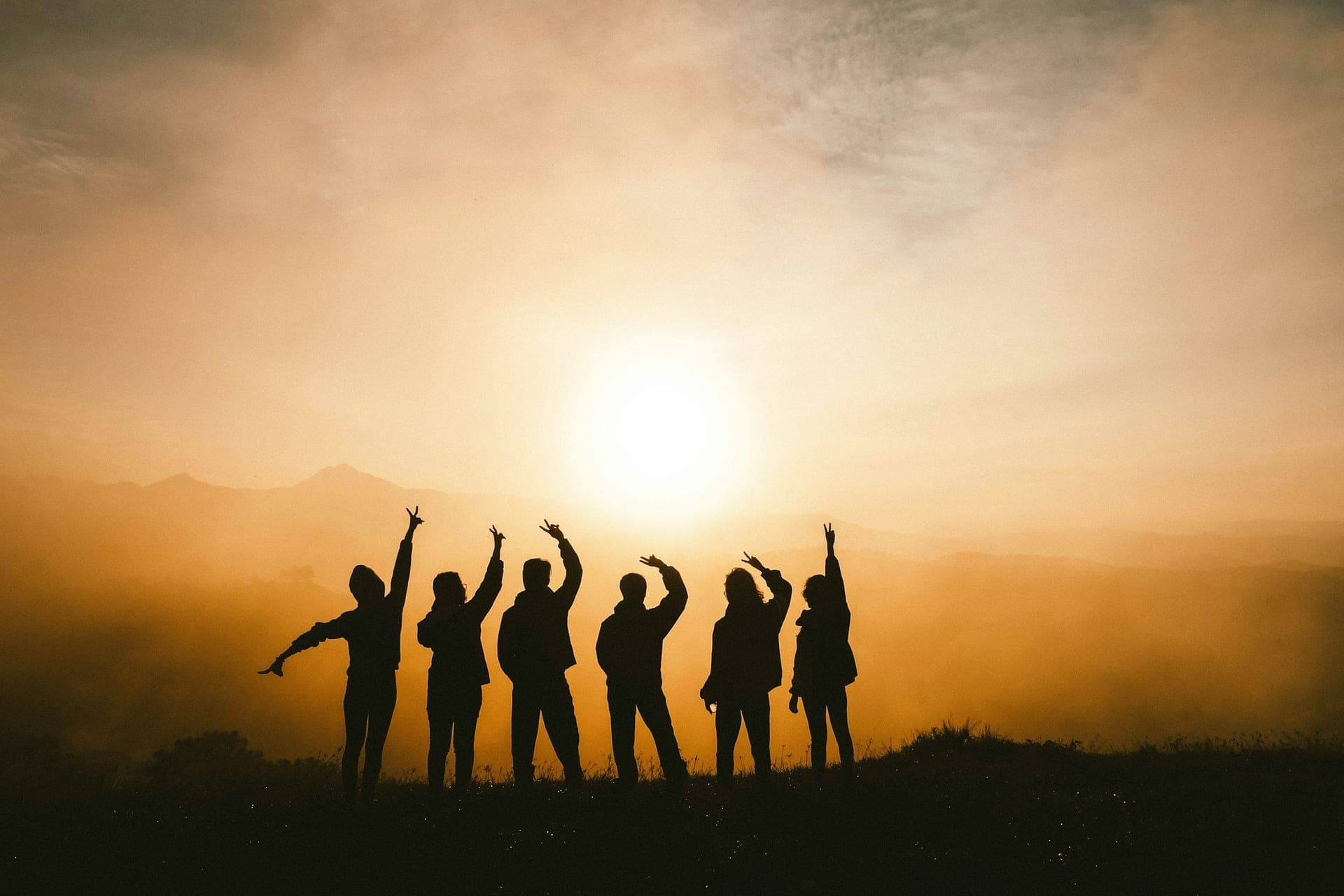 A group of friends silhouetted with arms raised against a warm golden sunset